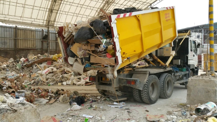 A yellow truck dumping trash at a facility.